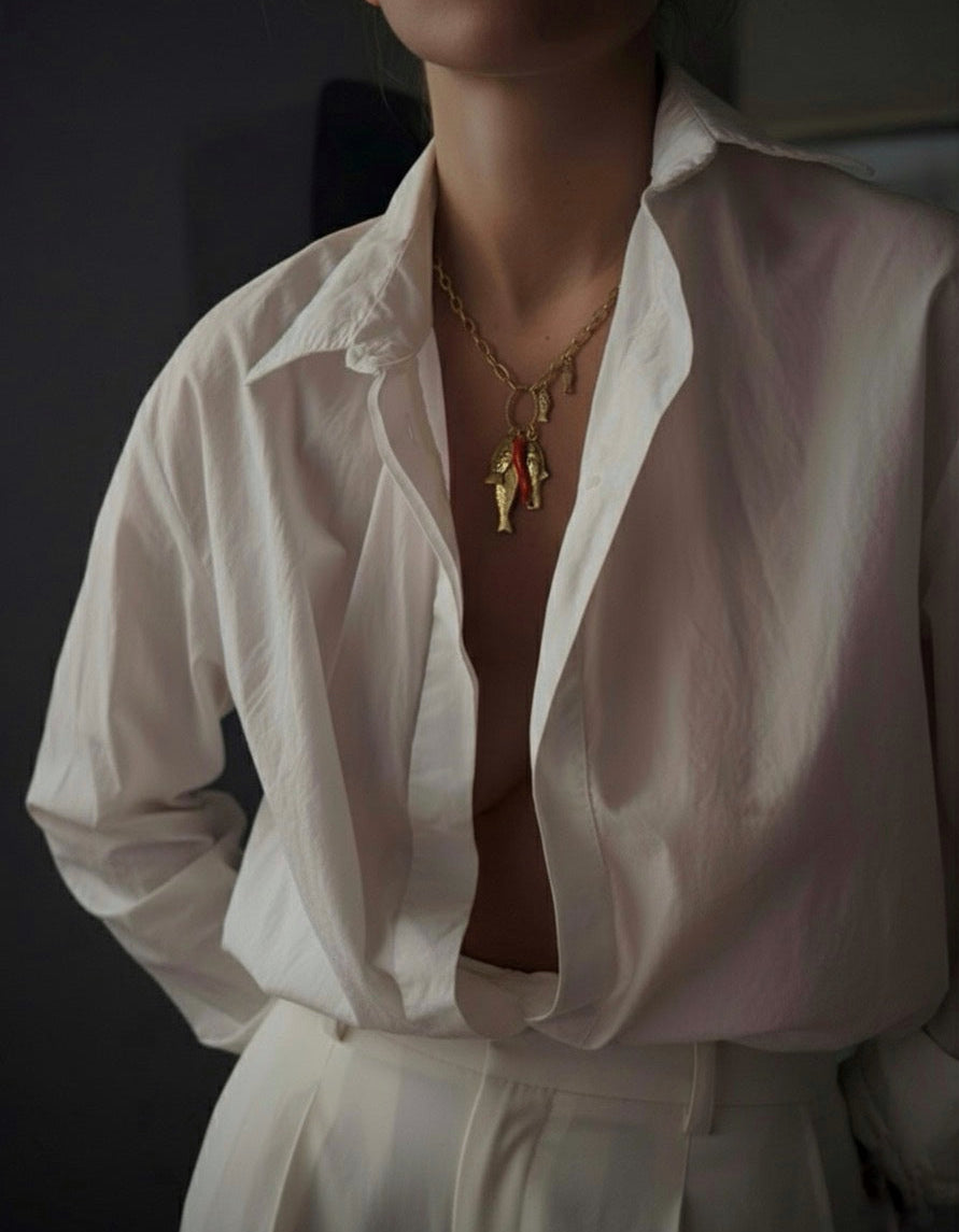 Person wearing a white shirt with a necklace featuring a fish pendant against a dark background
